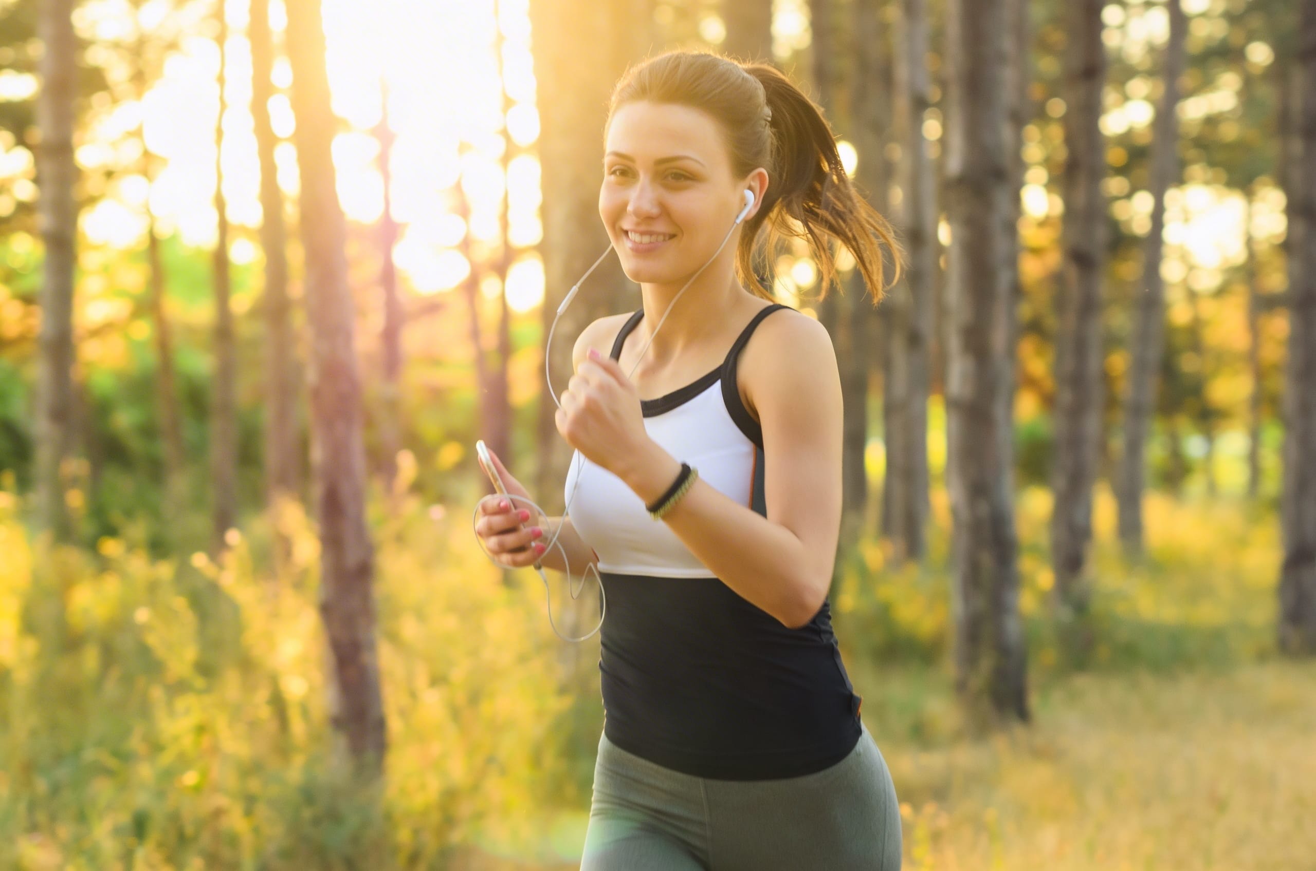 Woman jogging outdoors while listening to music, representing an active lifestyle supported by online nutrition and fitness coaching from a licensed dietitian and certified personal trainer